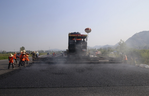 2019年8月，宜春經(jīng)開區(qū)S311路面攤鋪現(xiàn)場，工友們輔助路面兩側(cè)的分料、補(bǔ)窩等作業(yè)